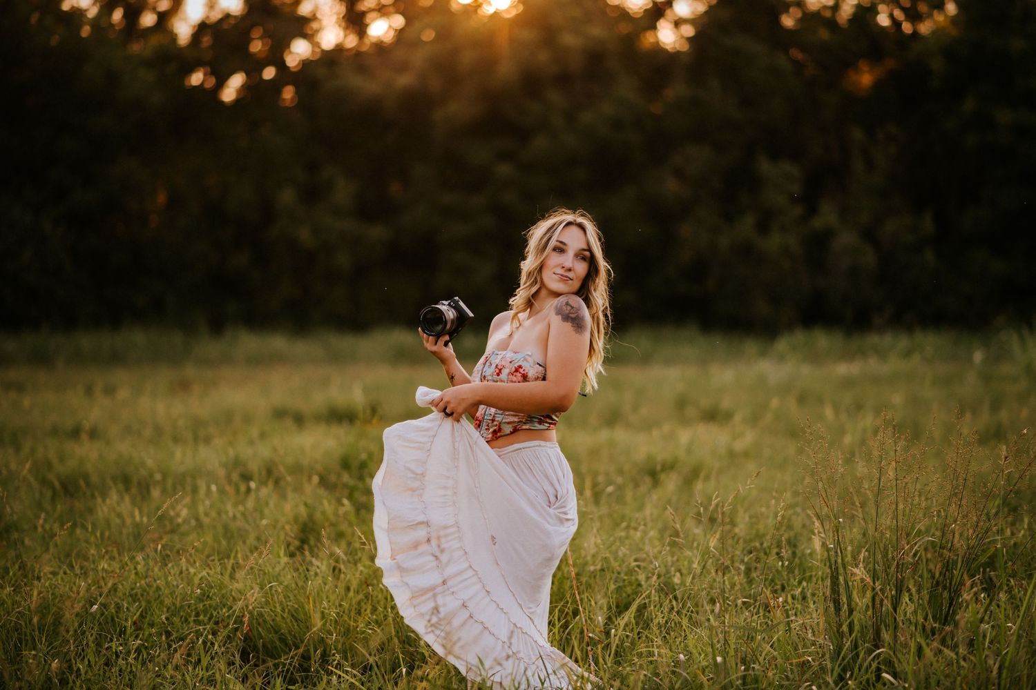 Branding photo of a photographer in a field at sunset with her camera in her hand as she plays with her skirt in Clarksville, Tennessee.