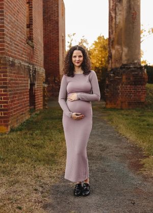 Pregnant mom dressed in a sleek purple dress hugs her baby belly at Barboursville Ruins, captured by Charlottesville maternity photographer.