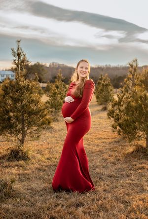 Pregnant mom dressed in siren red dress hugs belly against golden afternoon light, captured by Charlottesville maternity photographer.