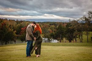 Expectant couple nuzzle together against a stormy autumn mountain backdrop, captured by Charlottesville maternity and baby photographer