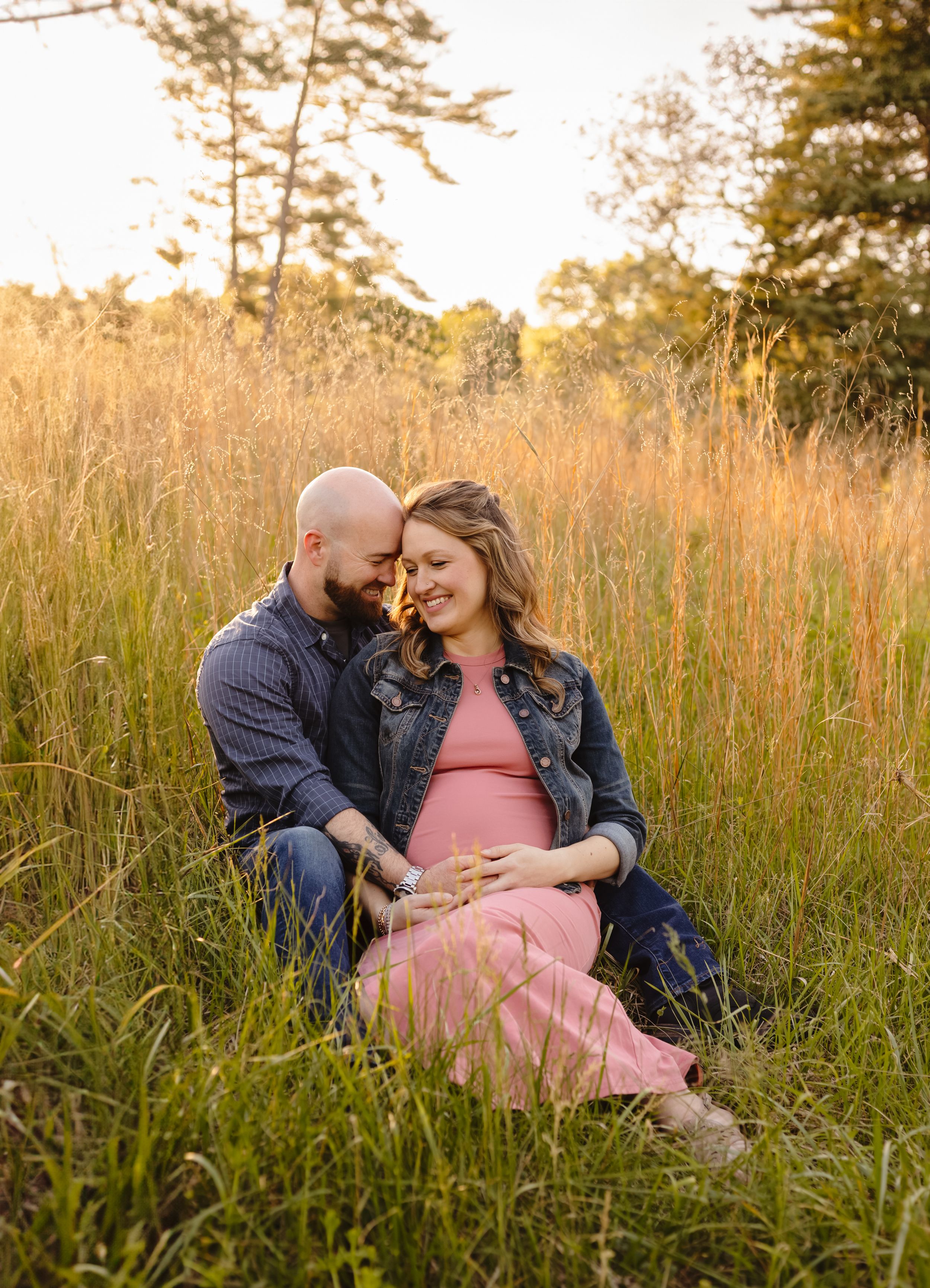 Parents-to-be snuggle up together in a field of tall grass at Boar's Head Resort, captured by Charlottesville maternity photographer.