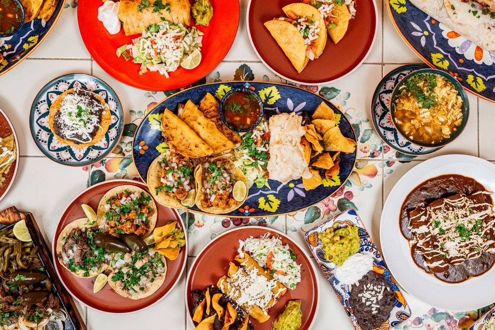 Colorful Mexican food spread featuring tacos, enchiladas, rice and beans served on traditional ceramic plates.