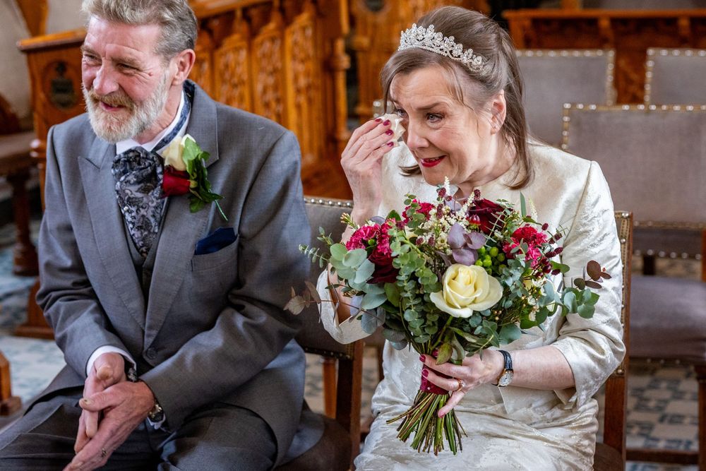Bride sits with bouquet, wiping happy tears beside the groom before the ceremony at Southport Town Hall wedding.