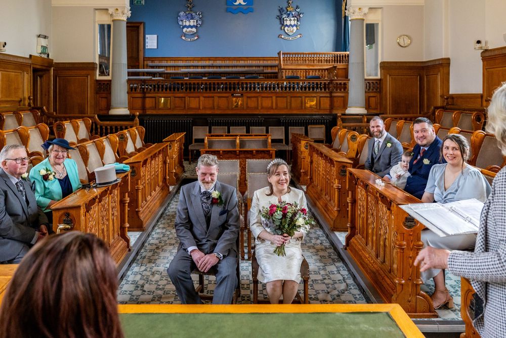 Bride and groom smiling during their wedding ceremony at Southport Town Hall surrounded by close family and friends.