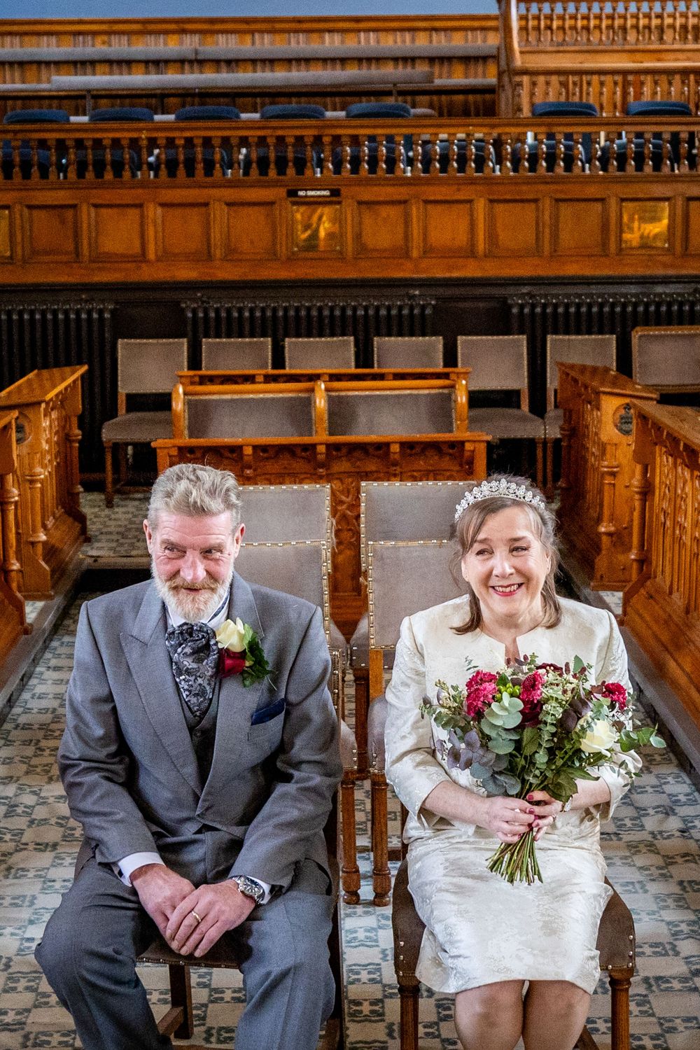 Bride holding her bouquet beside the groom inside Southport Town Hall just before their wedding ceremony begins.