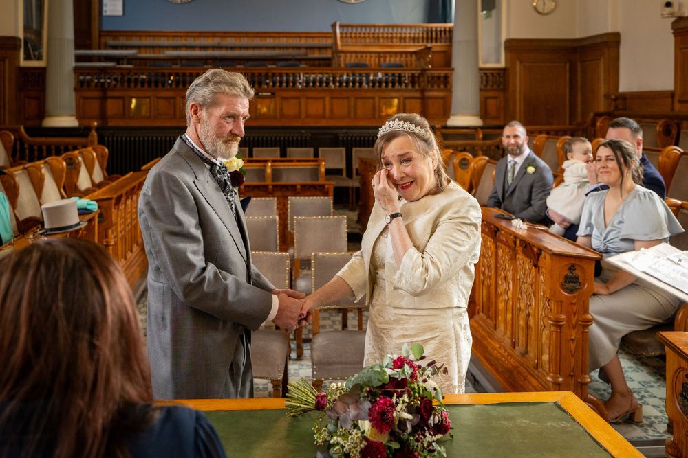 Bride wipes away happy tears while holding hands with the groom during their Southport Town Hall wedding ceremony.