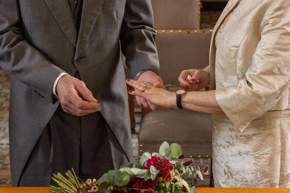 Groom places wedding ring on bride’s finger during intimate ceremony at Southport Town Hall, with bouquet on the table.