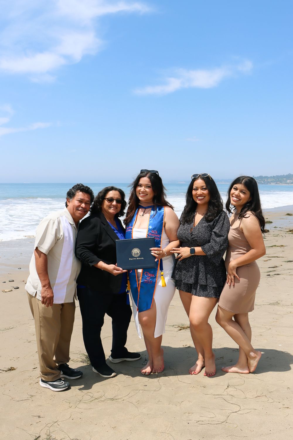 A group of friends pose together on a sunny beach with a diploma, celebrating graduation.