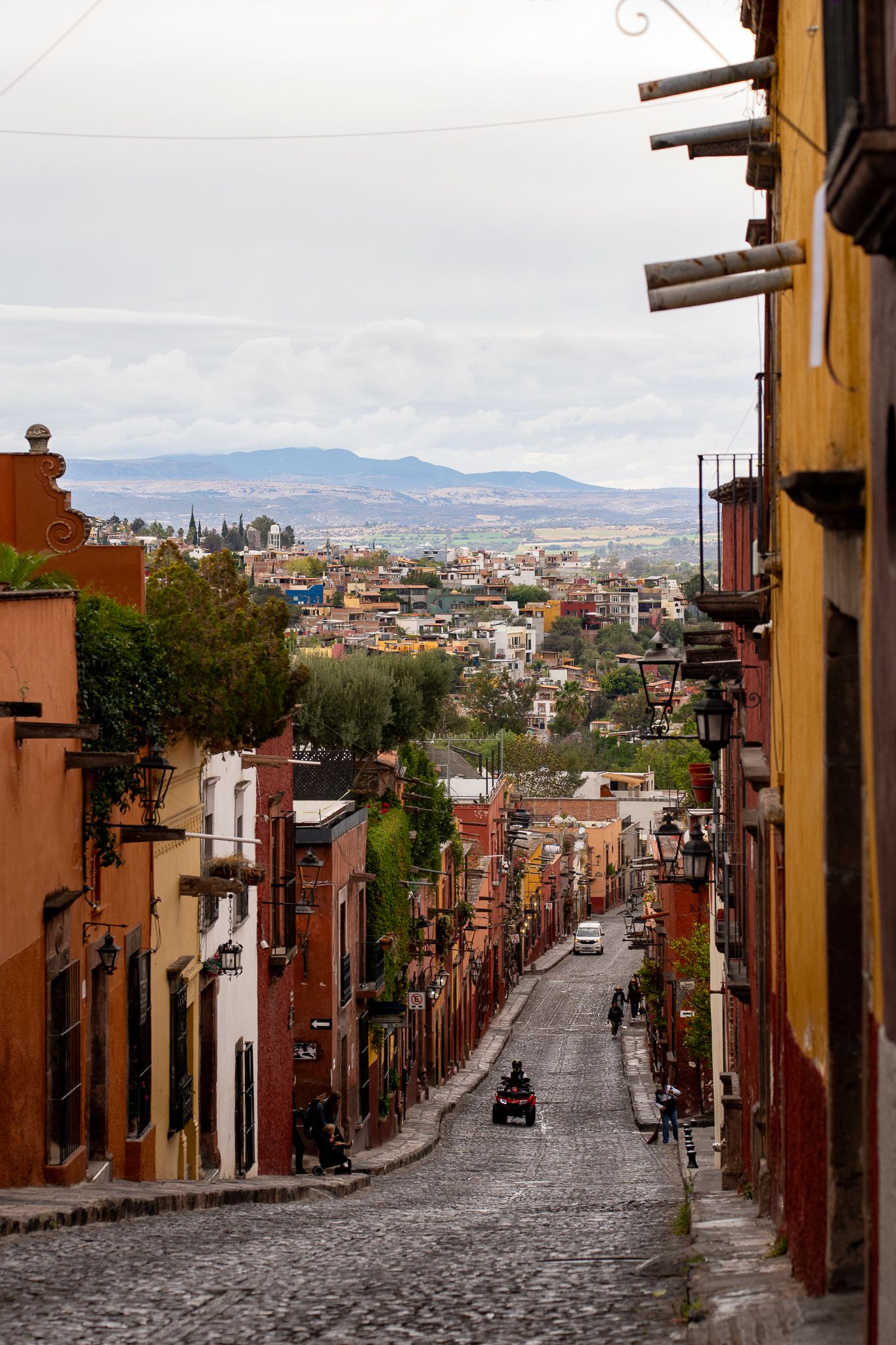 Steep cobblestone street lined with colorful colonial buildings in San Miguel de Allende, Mexico with mountain views.