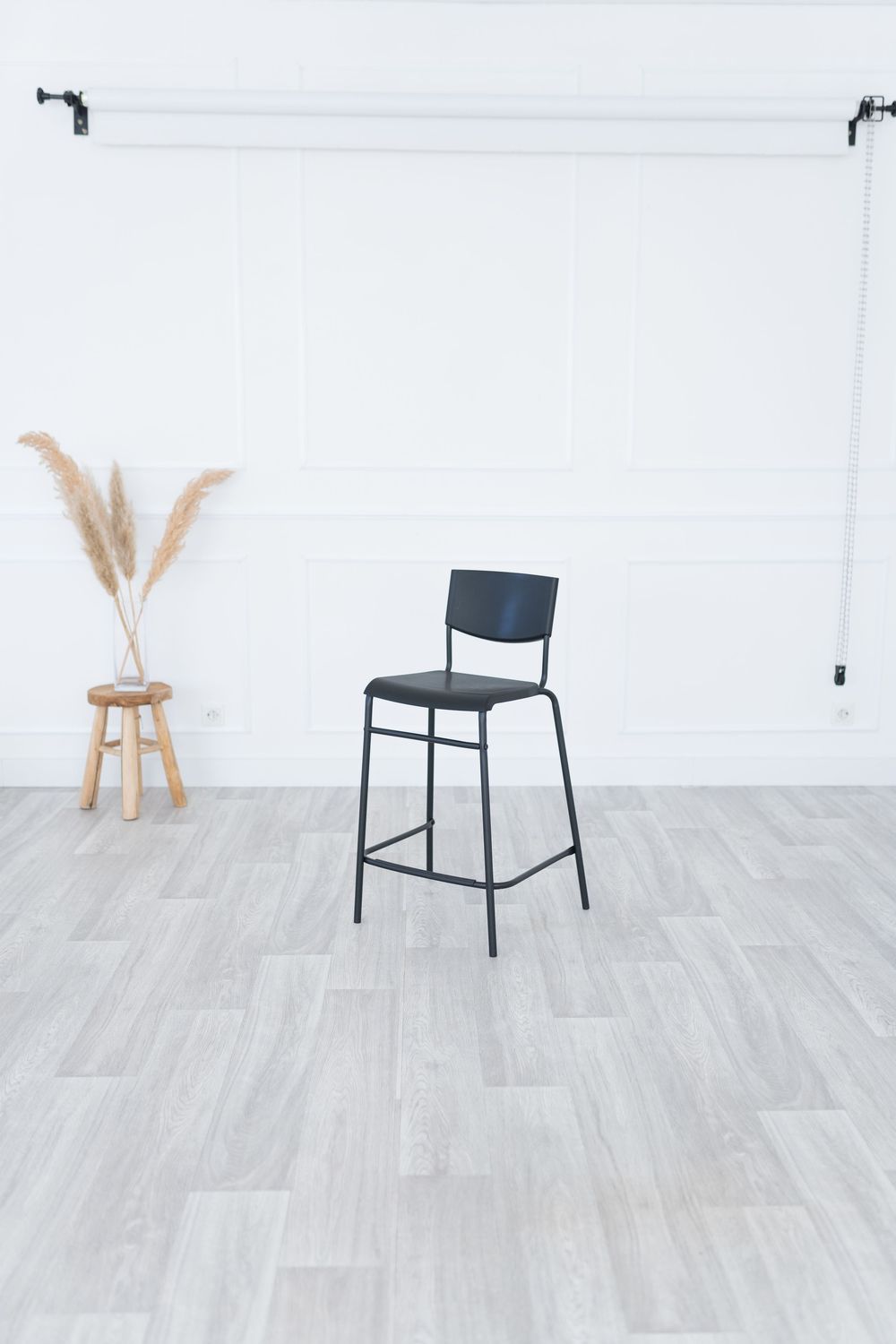 Modern black counter stool with upholstered seat and metal frame shown from different angles on light wood flooring.