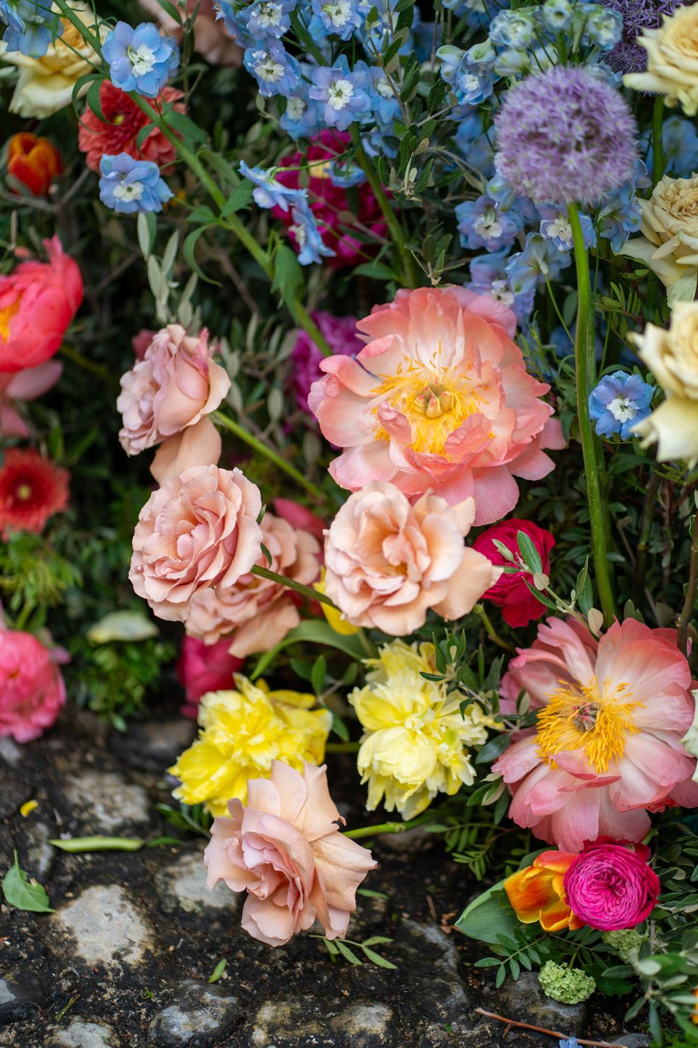 Pink roses and blue forget-me-nots bloom together in a colorful garden border against weathered stone.