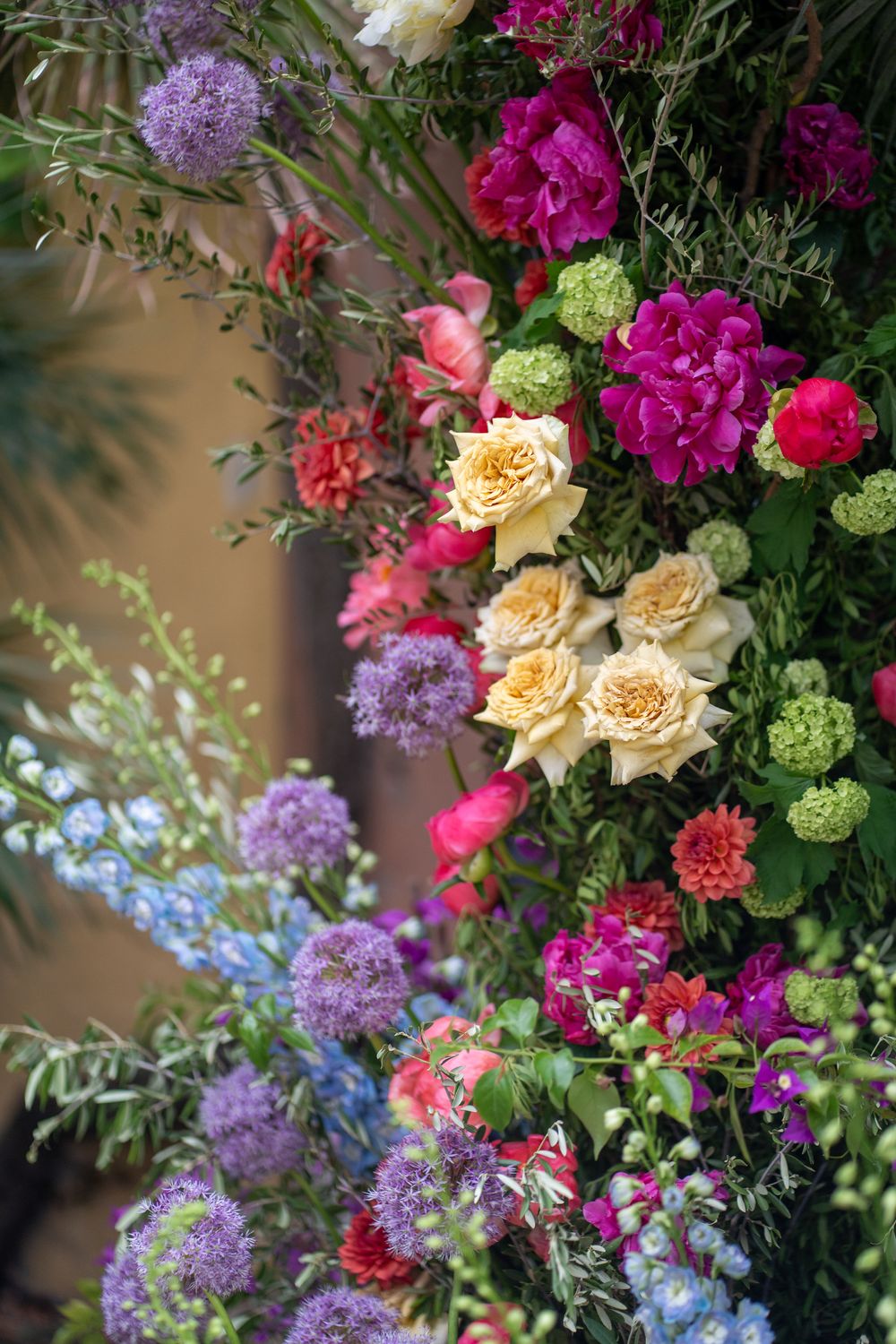 Vibrant floral arrangement featuring peach roses, purple lilacs, pink carnations, and green viburnum blooms against a soft background.