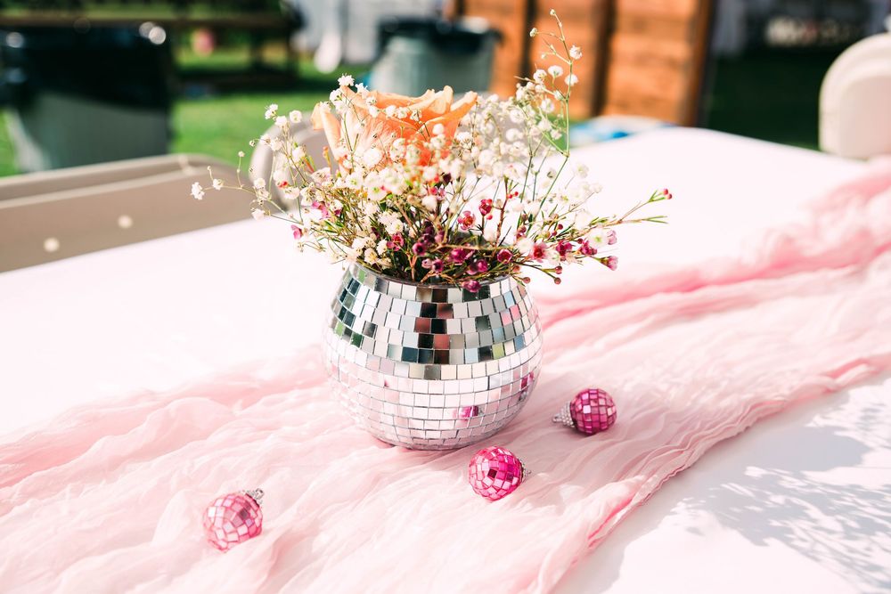 A disco ball vase with delicate pink flowers creates a sparkly centerpiece on a pink tablecloth.