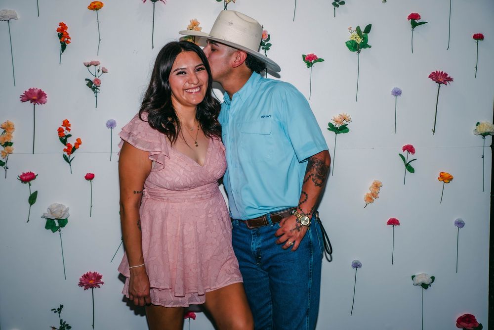 Outdoor party scene with floral wall decorations and people in casual attire.