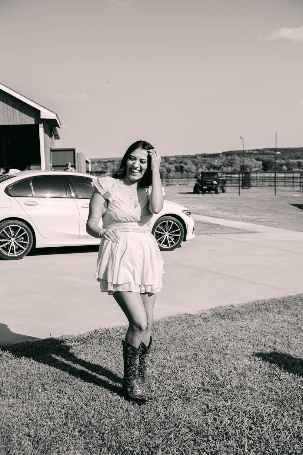 A black and white portrait in front of a car and rural building.