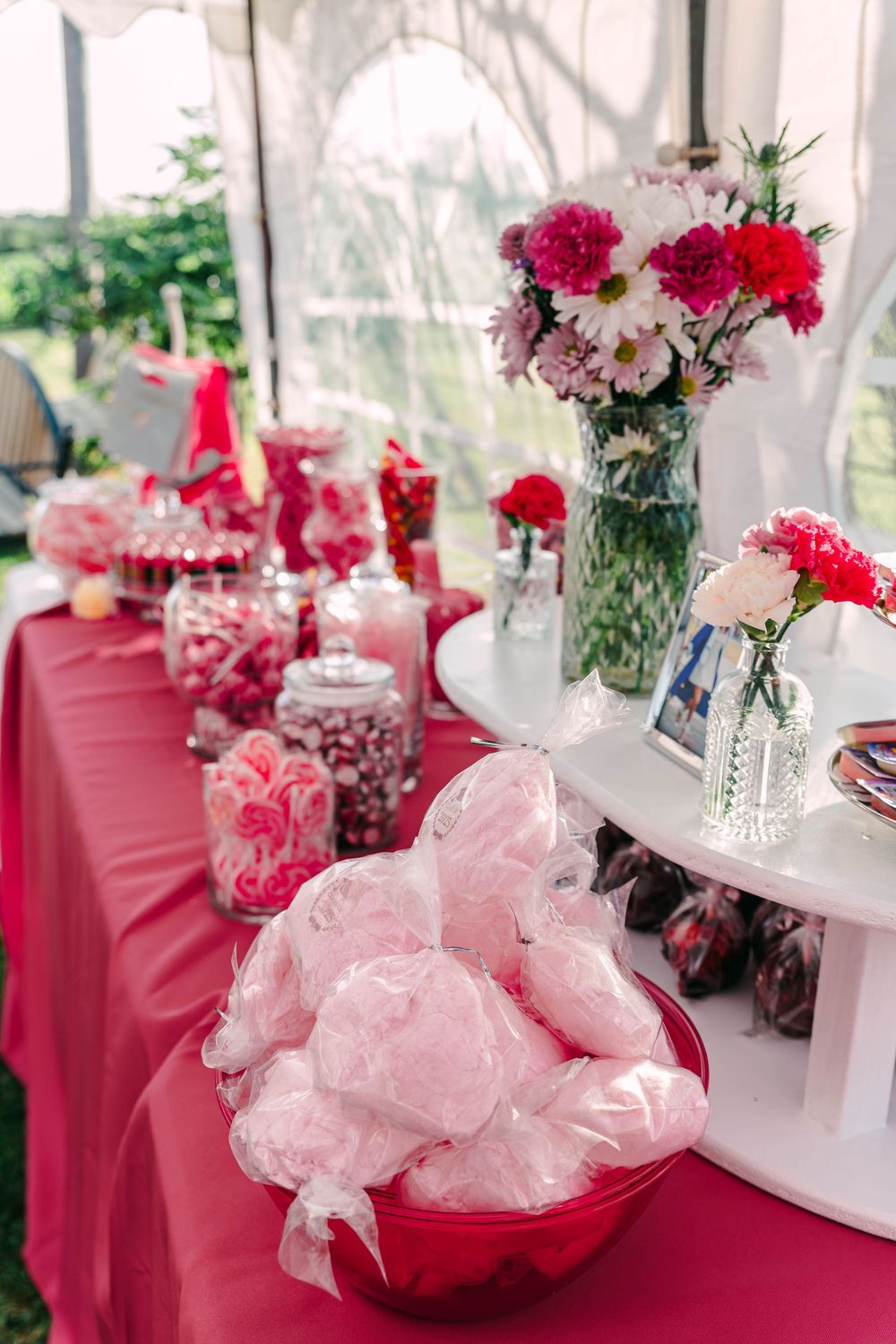 A candy and dessert table decorated in pink with flowers and glass jars.