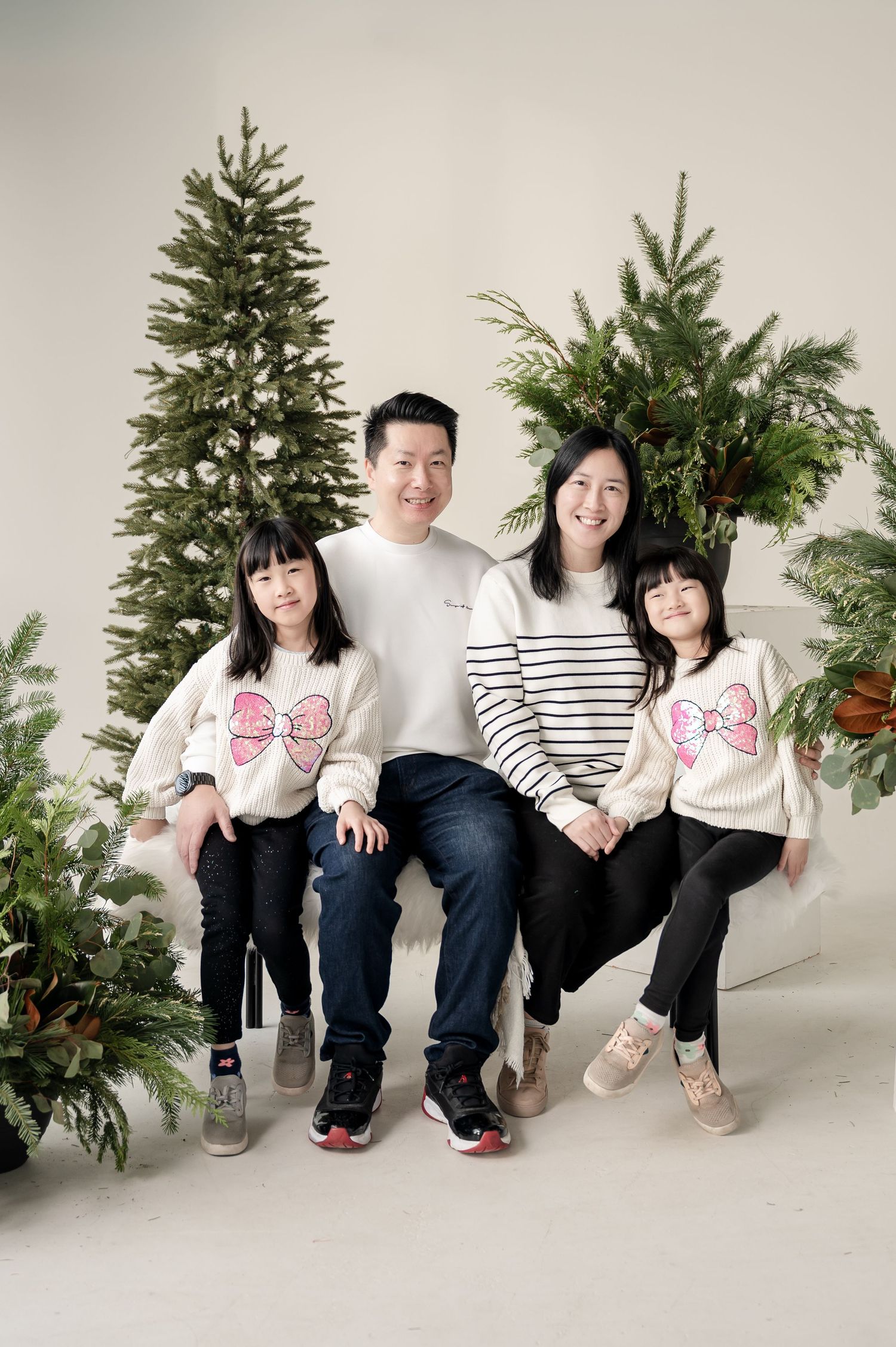 A family poses together for a holiday portrait with two evergreen trees in the background.