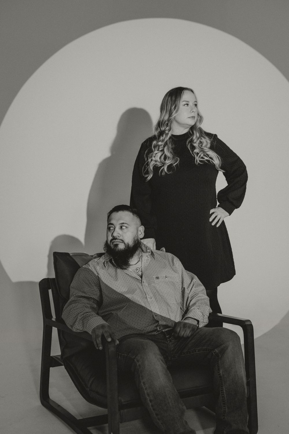 Black and white studio portrait of a couple posing against a circular backdrop with dramatic lighting.