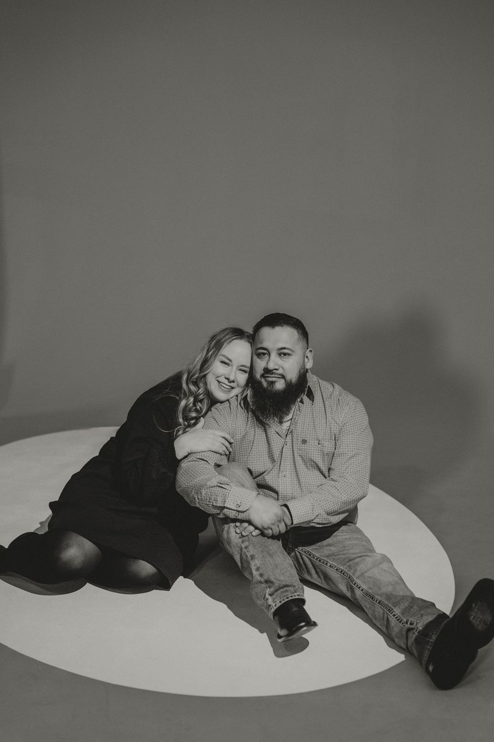 A series of black and white photos showing a couple laying on a white circular surface in different poses.