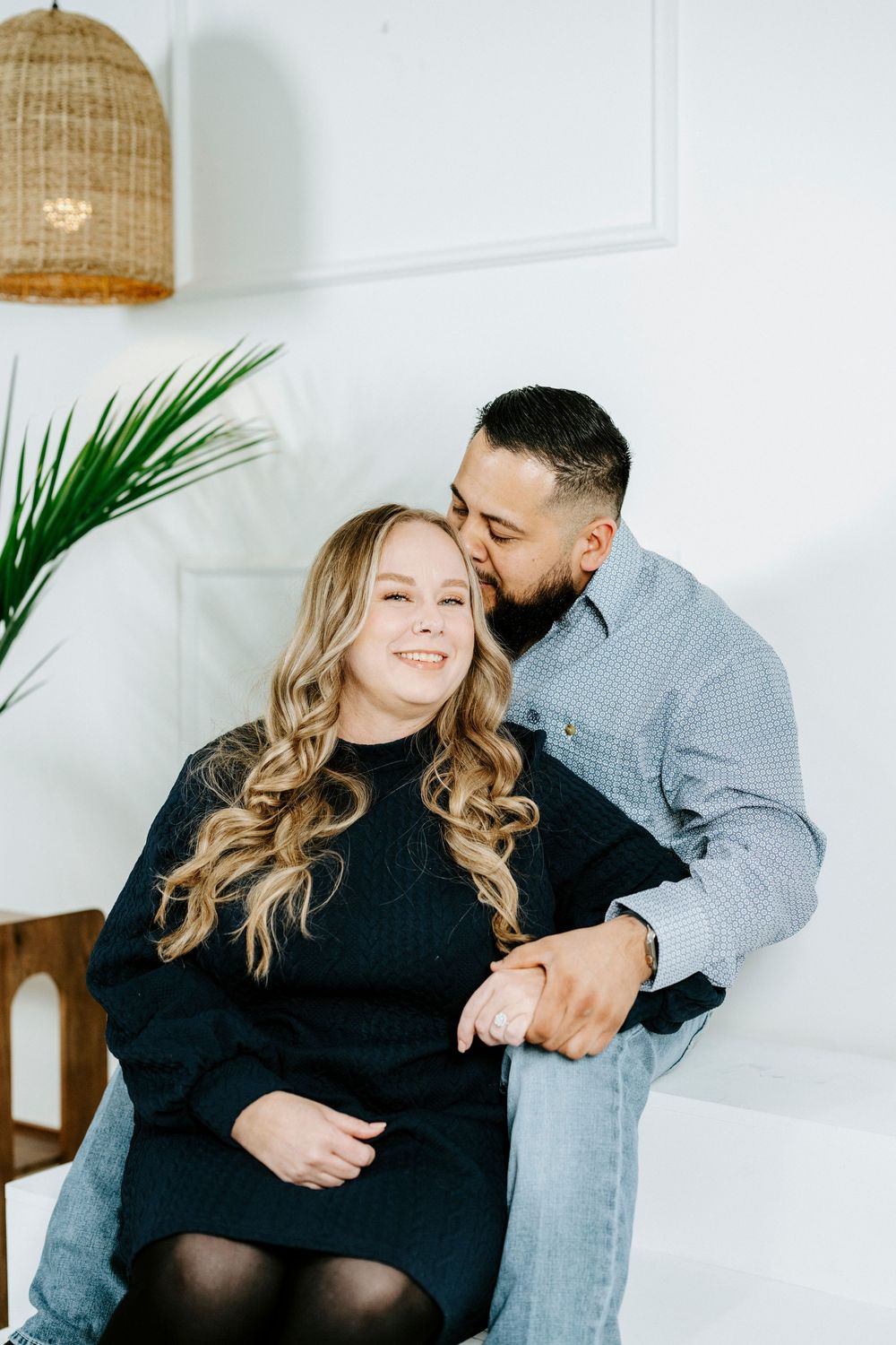 A couple shares tender moments together in a bright white room with a woven basket hanging above.
