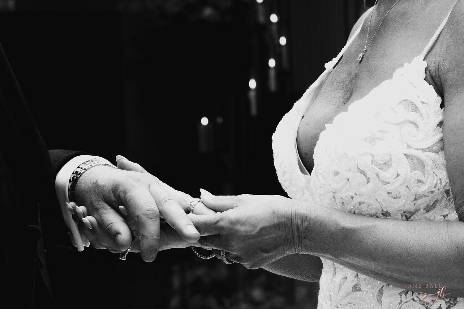 A black and white wedding photo showing hands exchanging rings during the ceremony.
