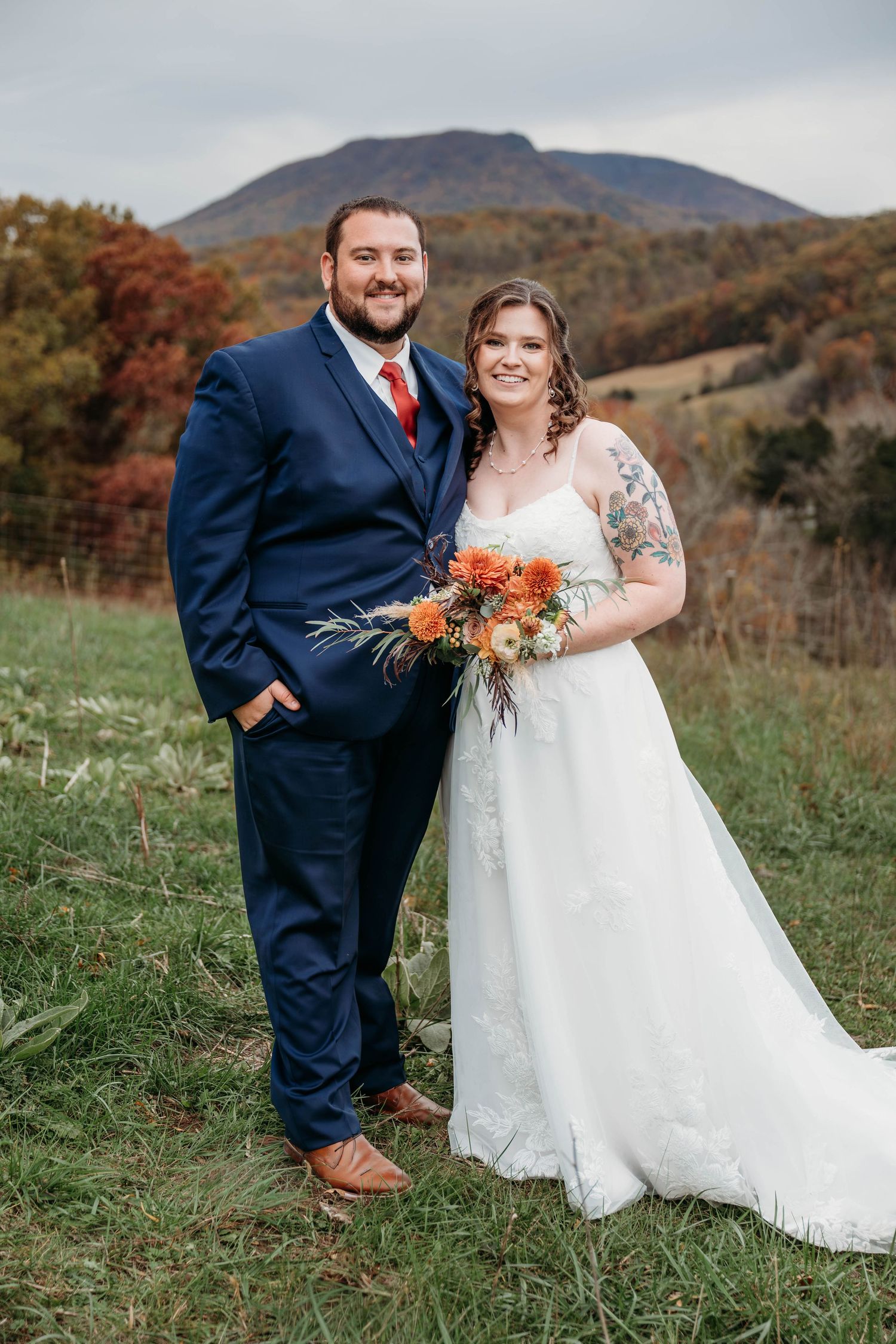 A wedding couple poses together in a scenic mountain meadow with fall foliage and rolling hills in the background.