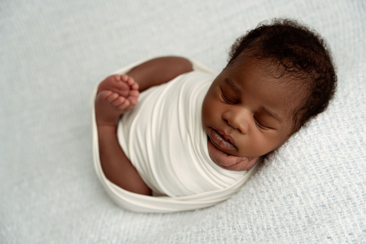 Sleeping newborn wrapped in white fabric lying in heart-shaped bowl with delicate headband on rustic background. – Paloma Schell