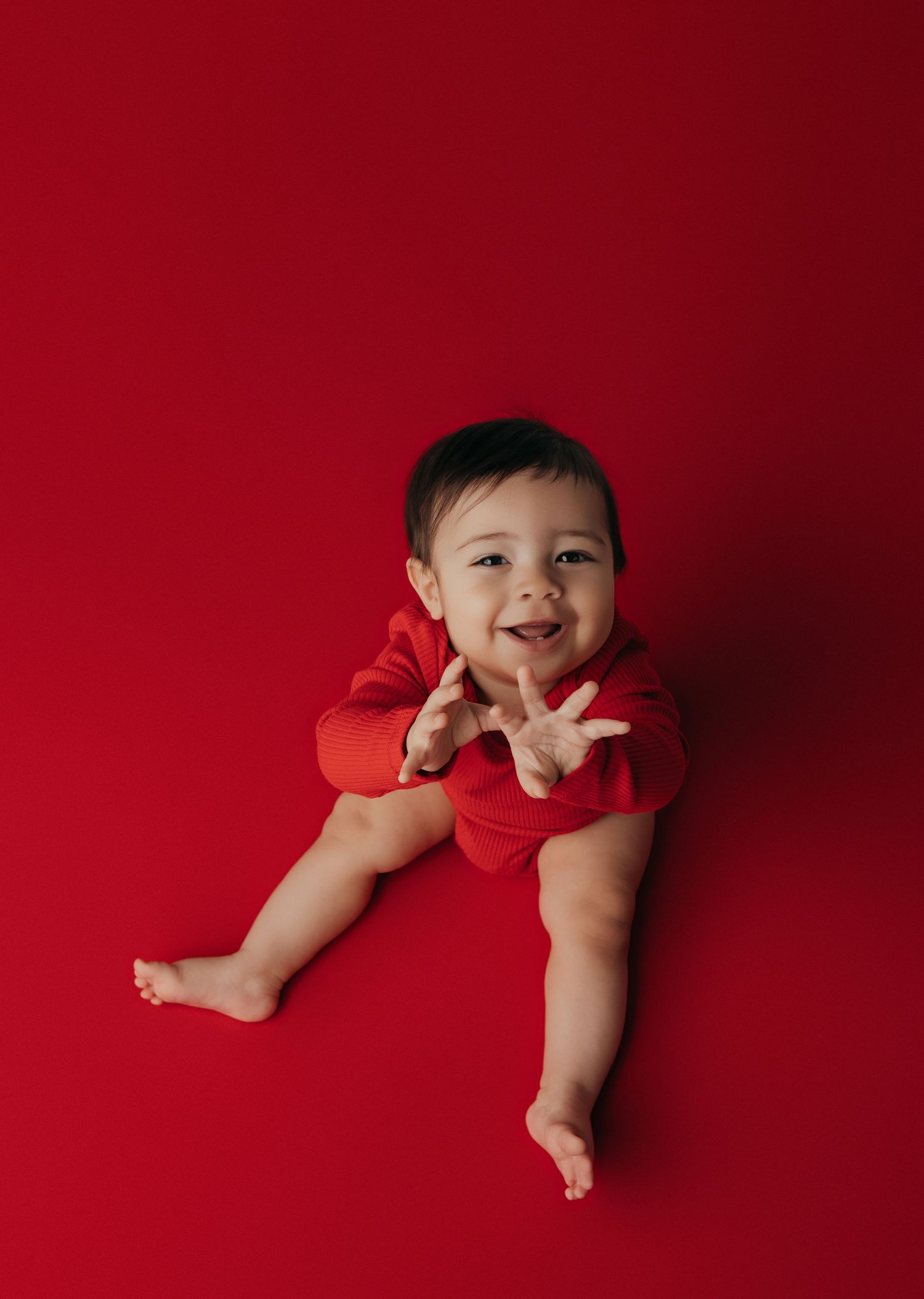 Baby photography session against vibrant red background showing playful poses.