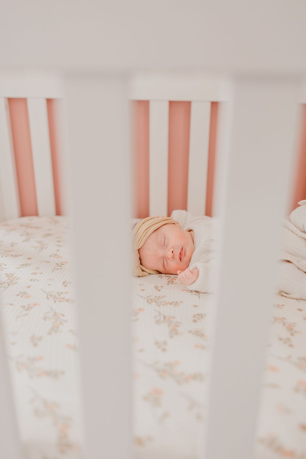 Sleeping newborn baby girl rests in her crib viewed through the crib slats.