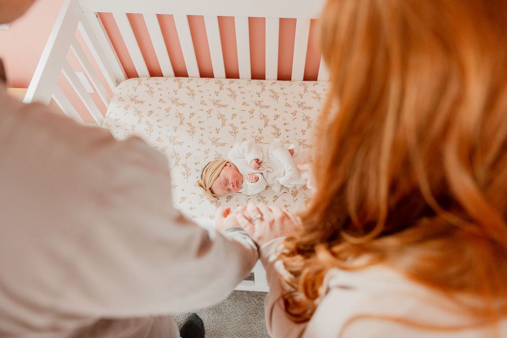 Parents look down at their sleeping newborn daughter resting in her crib.