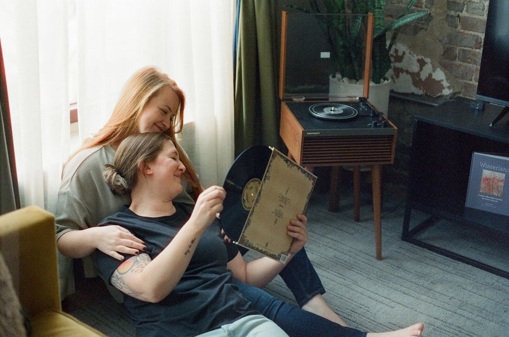Couple relaxing at home looking at vinyl record album near a retro turntable by a window.