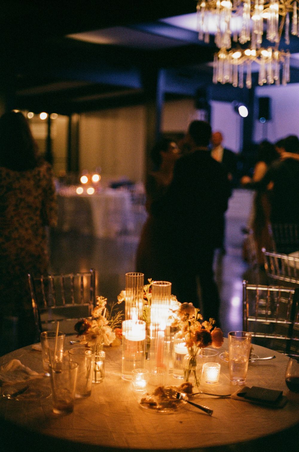 Romantic candlelit table settings at an elegant wedding reception with glowing centerpieces and crystal chandeliers overhead.