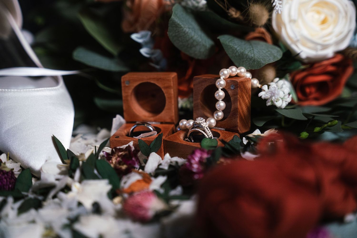 Wedding rings and jewelry boxes arranged with roses and white florals in soft lighting.
