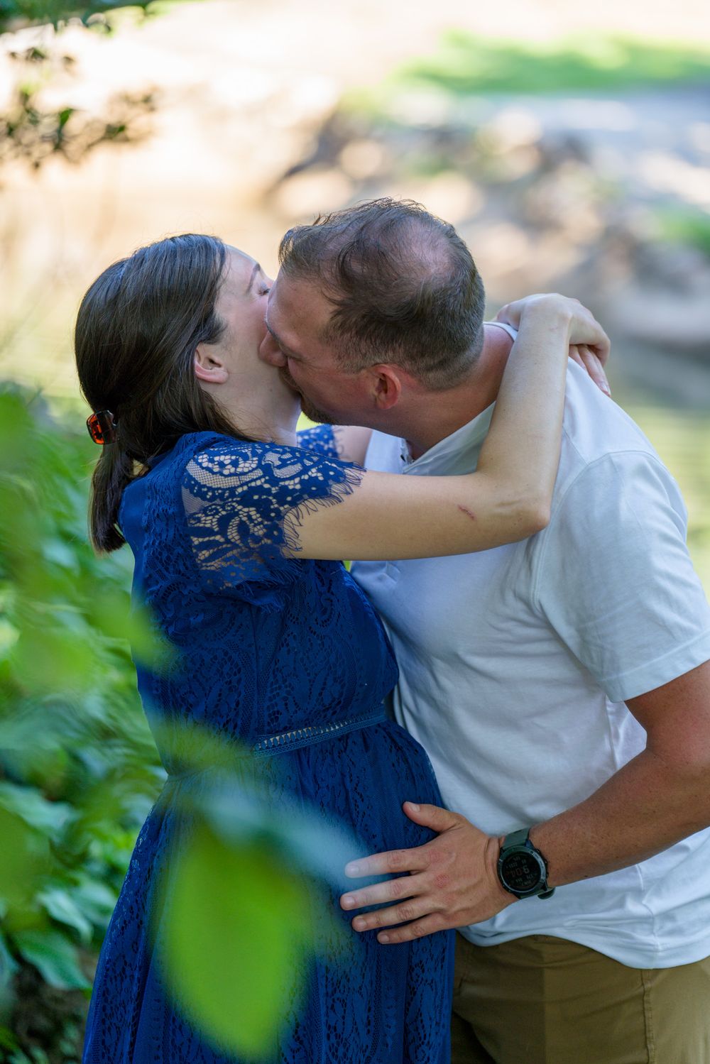 A romantic embrace in a garden setting with green foliage framing the scene.