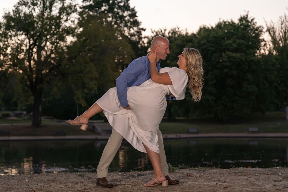 A romantic dip pose at sunset near the water's edge during an outdoor photo session.