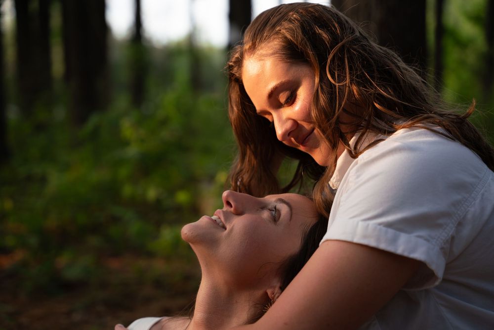 A romantic couple sharing a tender embrace outdoors during golden hour in a forest setting.