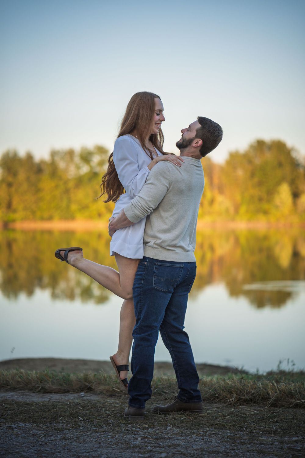 A couple shares a romantic moment by a serene lake at sunset, with golden light illuminating their silhouettes.