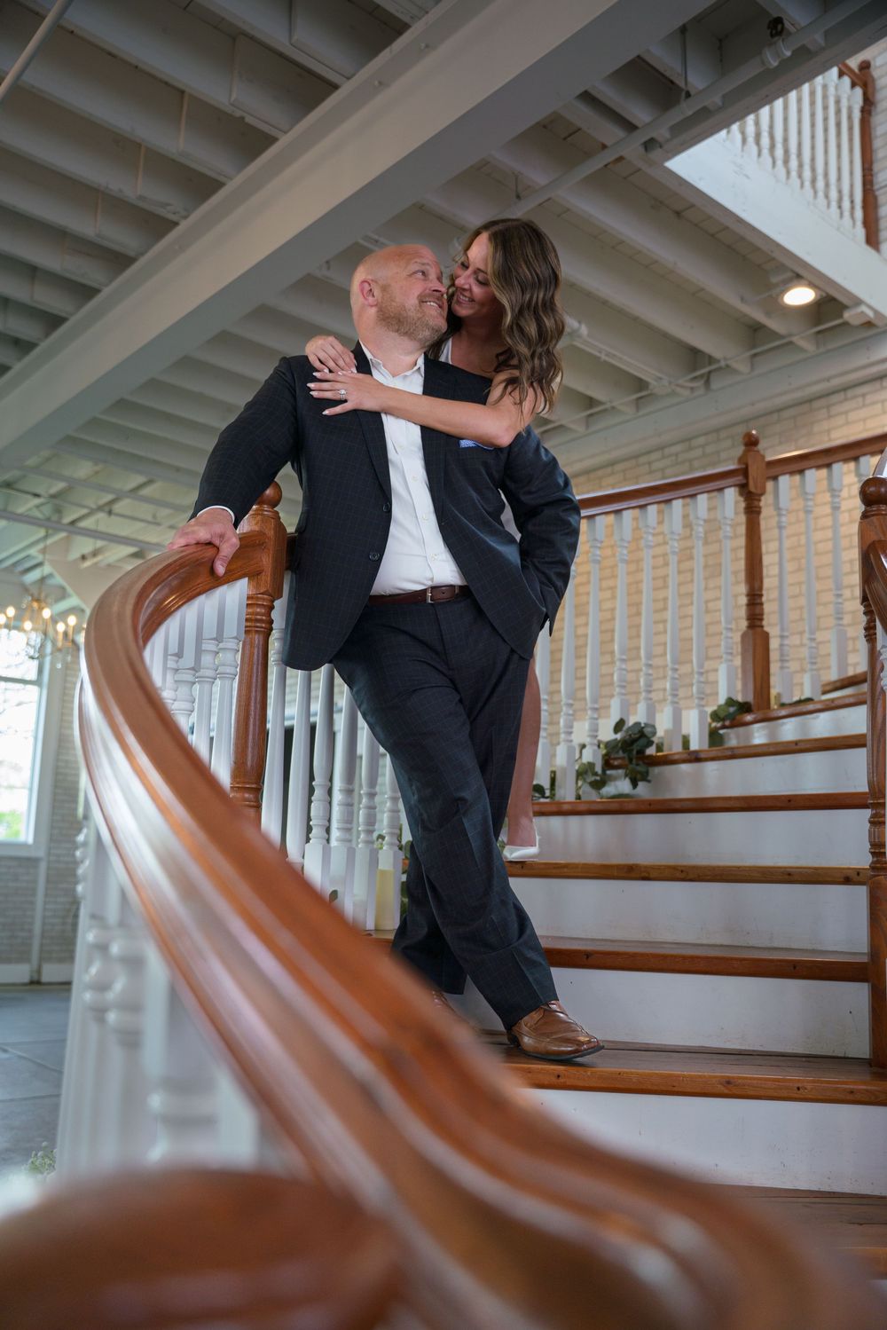 Couple shares romantic moment on wooden staircase with curved bannister, photographed from creative low angle.