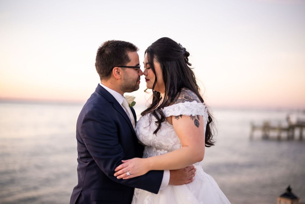 Close-up of newlyweds embracing on waterfront boardwalk during golden hour.