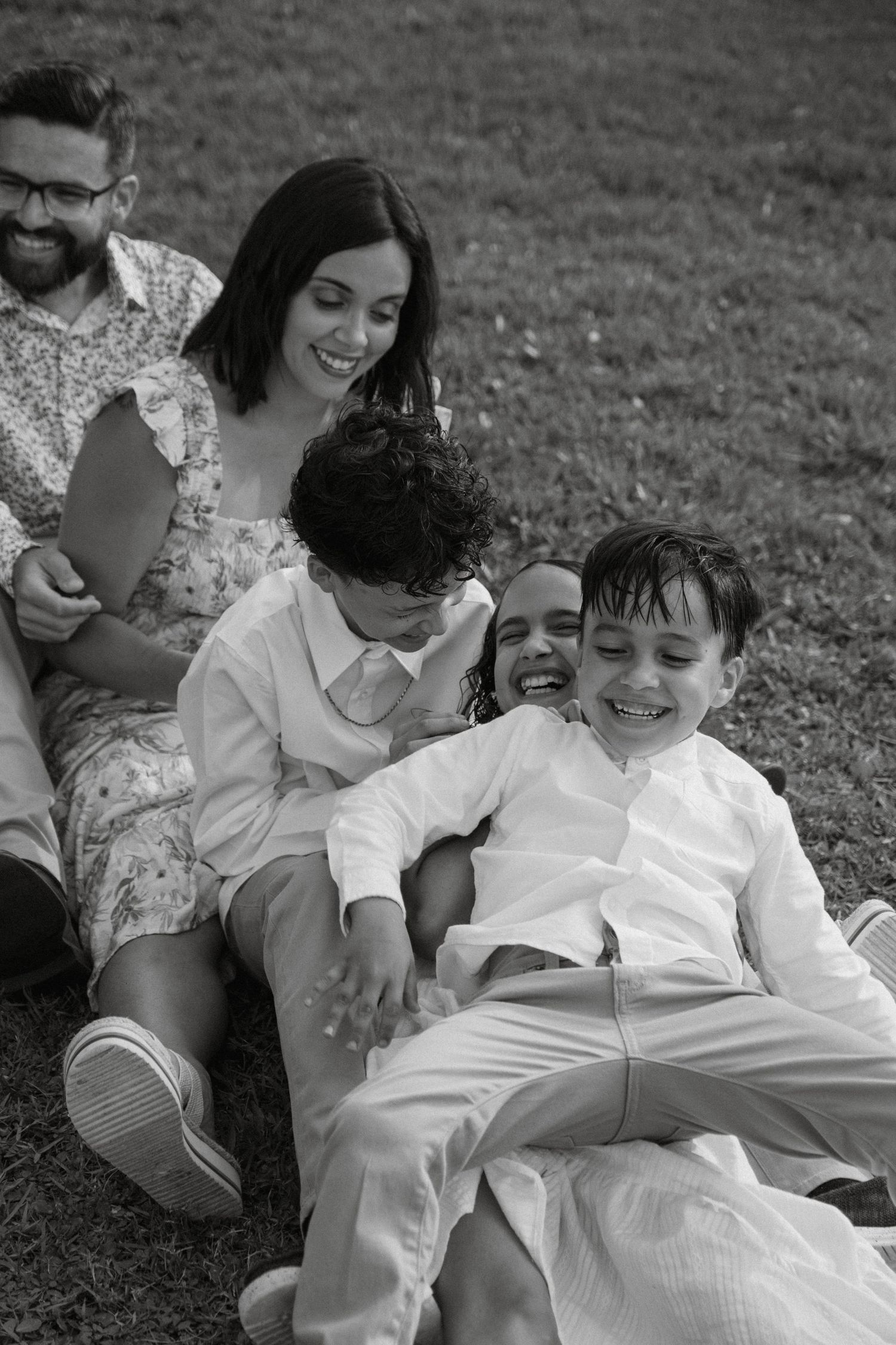 A group laughs together while lying on grass during a casual outdoor photoshoot.