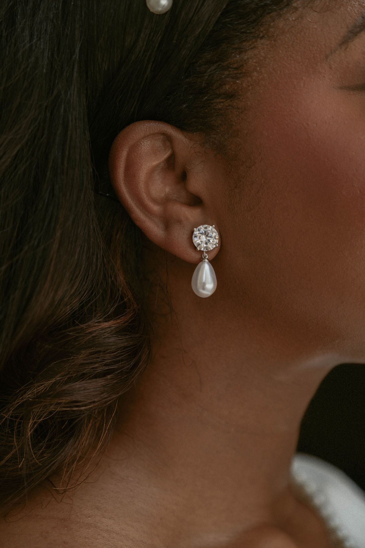 Close-up shots of elegant pearl and crystal drop earrings against a dark background.