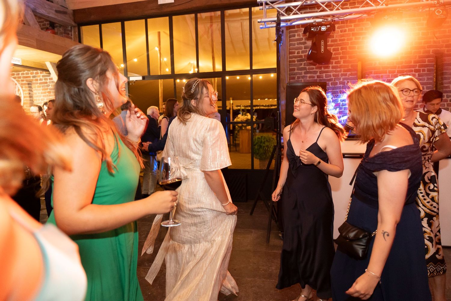 Wedding guests dancing and having fun at a reception with mood lighting and industrial decor.