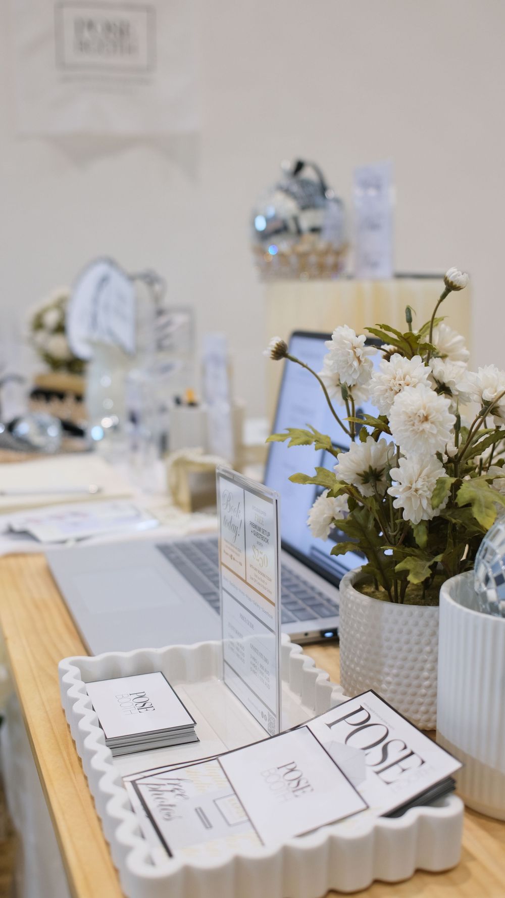 Photo booth setup with white scalloped trays, floral arrangements, and printed materials. Perth WA Photo booth Hire Event Booth