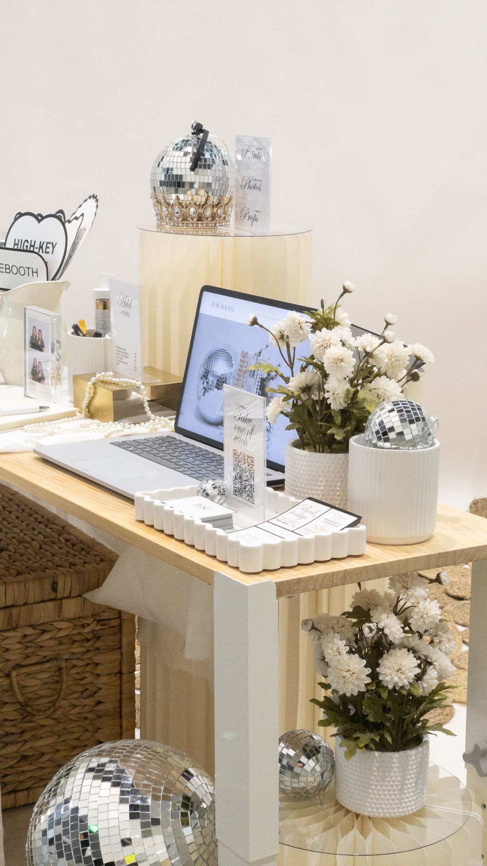 Modern photo booth setup with laptop, disco balls, and white floral arrangements on wooden desk. Perth WA Photo booth Hire Event Booth