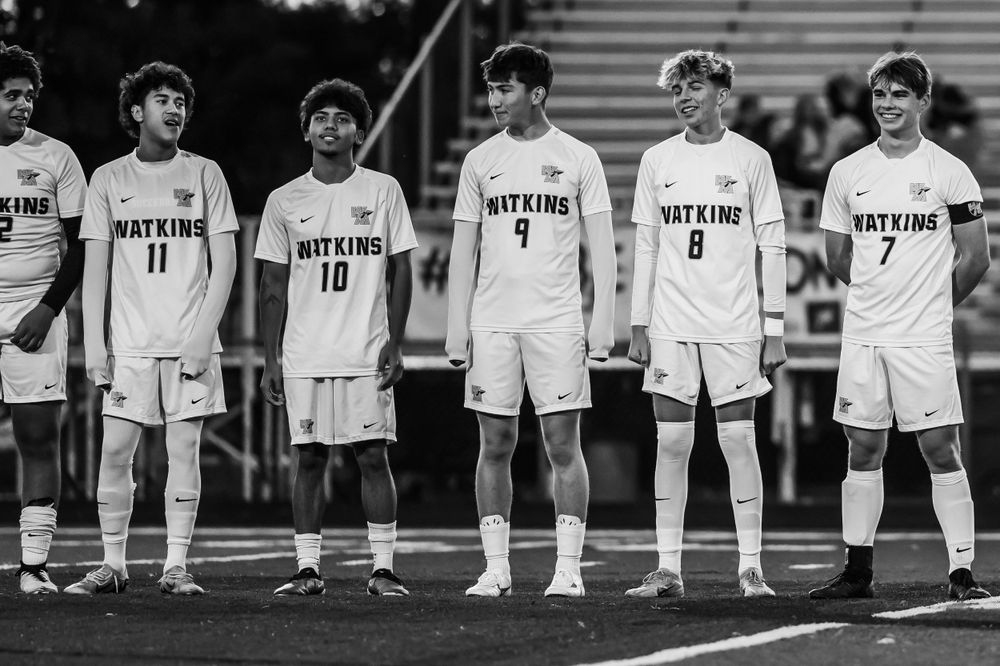 Soccer team lines up on field wearing matching white uniforms.