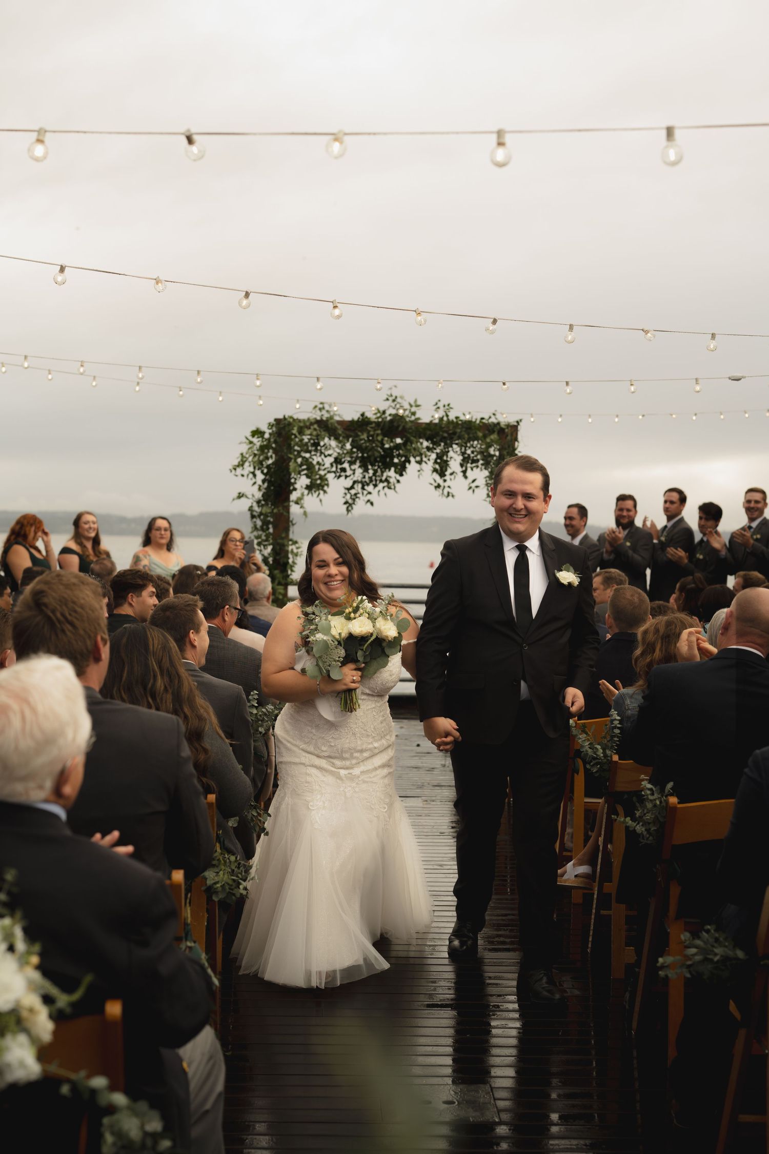 Wedding ceremony setup with string lights and floral arch overlooking waterfront.