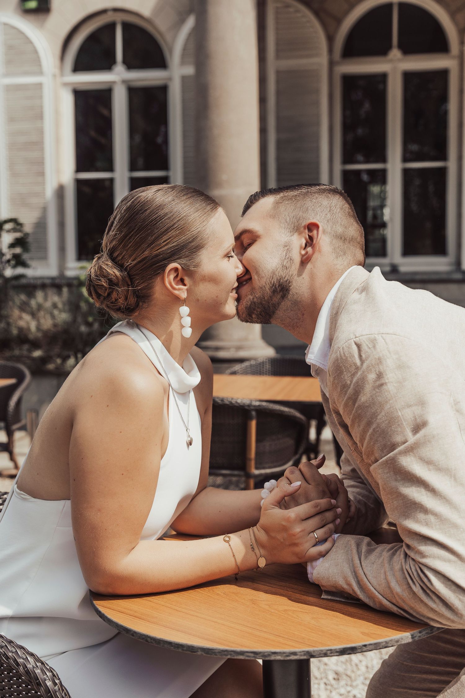 Intimate moment shared at outdoor cafe table with arched windows in background.