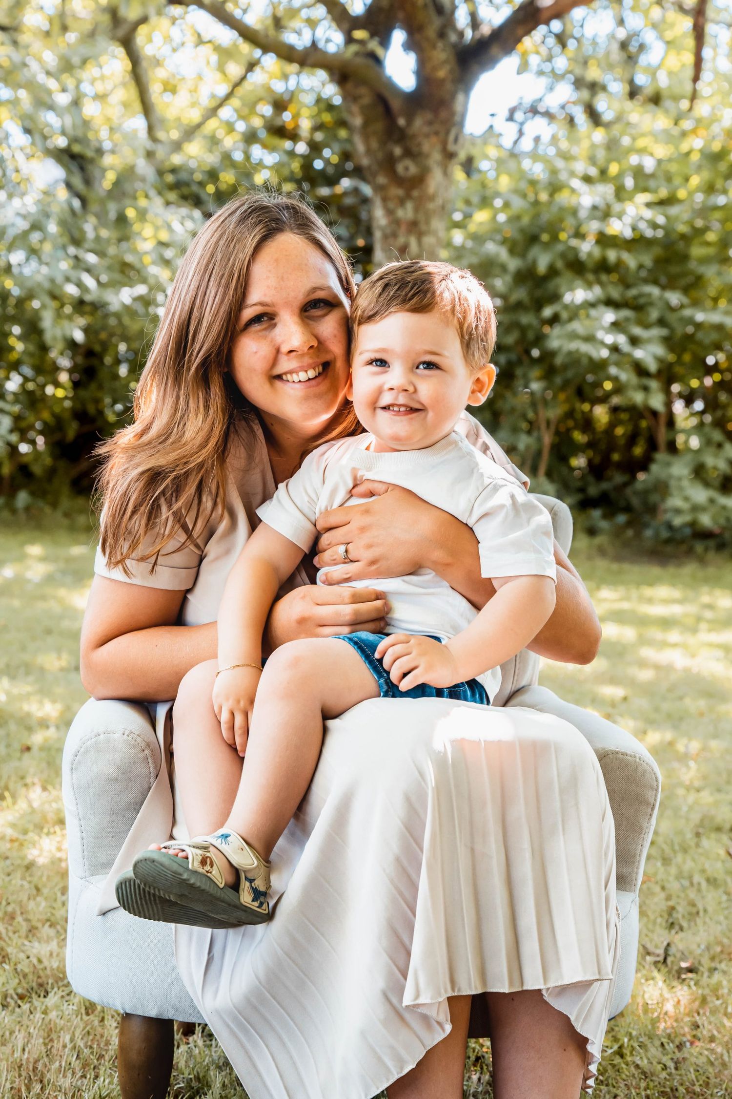 Mother and child sharing joyful moment on white chair in backyard garden setting.