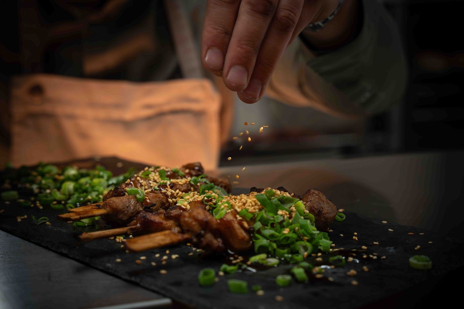 Chef garnishing a cooked dish with fresh herbs and spices on a dark slate plate.