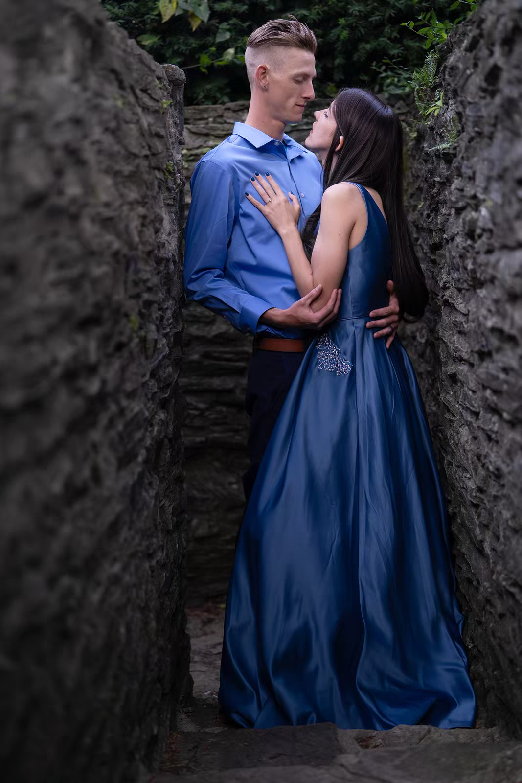 Romantic engagement photos against rustic stone walls in blue coordinated outfits.